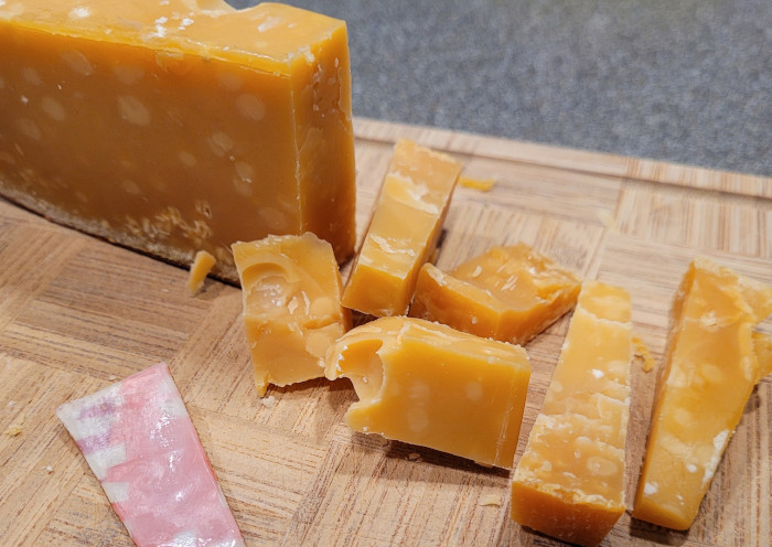 Photo of cheese wedge with crumbly slices and a piece of the wax rind in the foreground.
